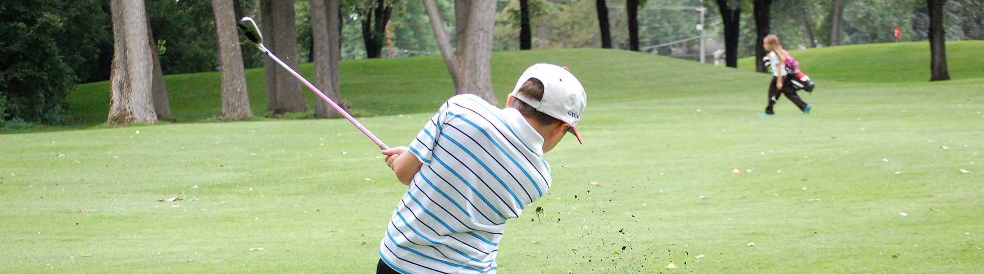 The back of a boy in mid swing on the golf course.